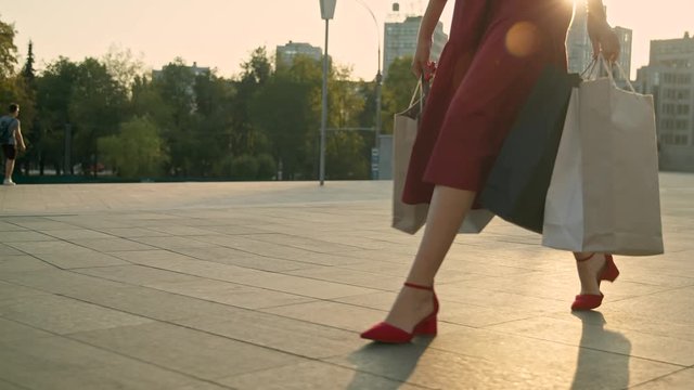 Young woman in red dress with shopping bags walks on the street during sunset