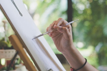 Close up of hand holding paintbrush and painting an abstract picture neary the window with natural background.