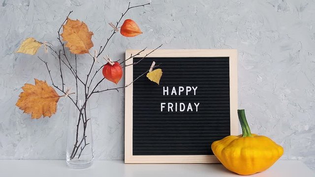Happy Friday text on black letter board and bouquet of branches with yellow leaves on clothespins in vase on table Template for postcard, greeting card Concept Hello autumn Friday.