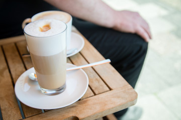Glas Latte Macchiato und Tasse Cappuccino Kaffee mit Milchschaum auf Holztisch draußen im Straßencafé 