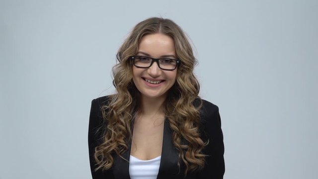 Business woman coquettishly smiling while looking at camera on gray background, slow motion