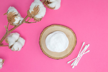 Cotton branch, pads on round wooden stand, ear sticks on bright pink background. Cosmetology, healthcare concept. Flat lay, top view, mock up, copy space, layout design