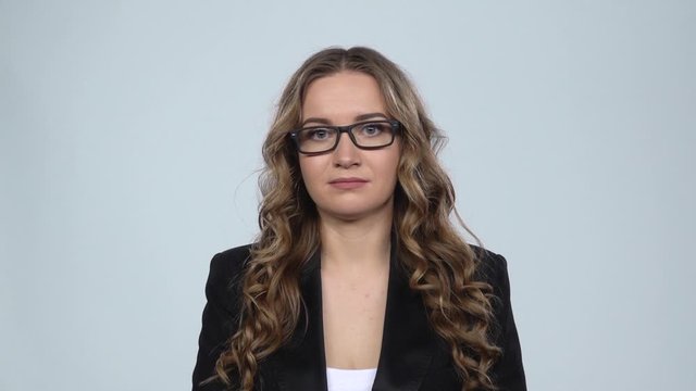 Woman disappointed looks in camera bites her lip then shrugs against grey background, slow motion