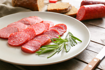 Plate with slices of different smoked sausages on wooden table