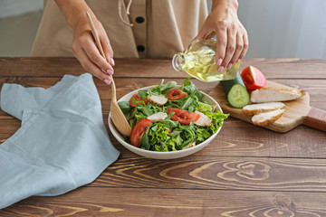 Woman preparing tasty arugula salad on table in kitchen