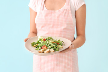 Woman holding plate with tasty arugula salad on color background, closeup