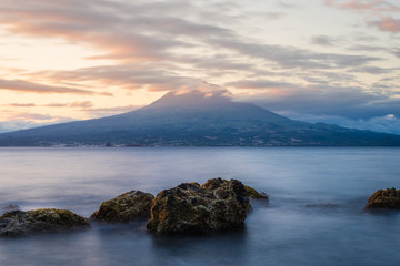 Fototapeta na wymiar Sunrise in Almoxarife, Horta, Faial island: Spray of splashing waves and the Volcano of Pico Mountain in the background, Azores Islands, Portugal 