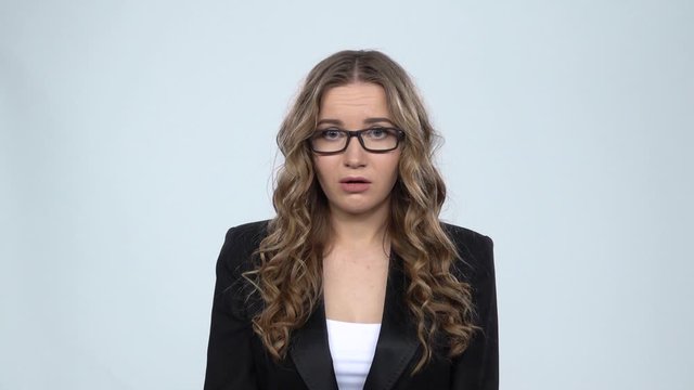 Girl in glasses looks upset at camera asking for something against grey background, slow motion