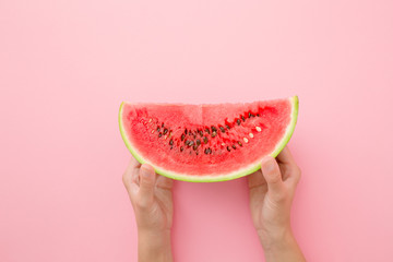Young woman hands holding red piece of watermelon on light pastel pink table. Closeup.