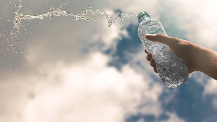 Hand holding a clear plastic bottle of pure drinking water refreshing and splash on a hot background with a hungry and thirsty concept for good health.