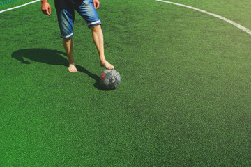 European football, lack of money for sports shoes and a new ball. Football player without shoes and an old ball, on a green new artificial field.   
