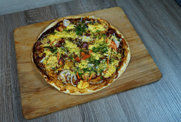Pizza with mushrooms, sausage cheese and herbs, on a table on a wooden board.     