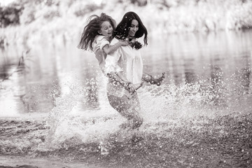 Mother and daughter run and have fun in the water with many splashes.