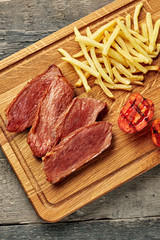Steak with French fries and grilled cherry tomatoes on a cutting board. Classic meat meal with red wine on an ethnic tablecloth. Top view, directly above.