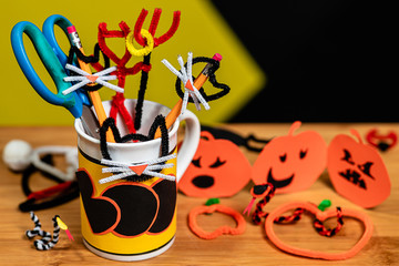 Office supplies decorated for Halloween in a Coffee Mug that says BOO. The table surface is covered in other halloween crafts.  Negative space for Copywriting.