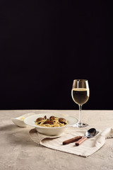 delicious Italian spaghetti with seafood served with white wine and grated cheese on napkin near cutlery isolated on black