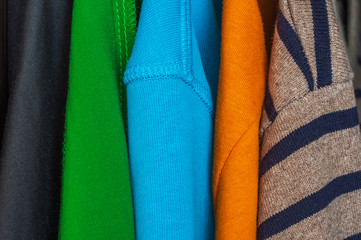 Multi-colored sweaters, dresses and body shirts hang in one closet.