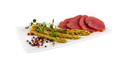 A small plate with asparagus, herbs and cured sausage on a white background.