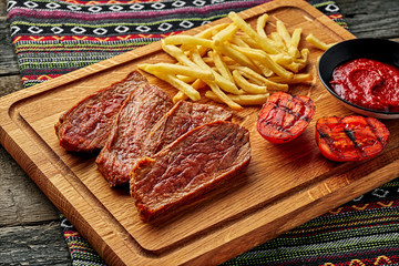Medium rare sirloin steak with chips and red wine on a rustic wooden table with ethnic tablecloth. Classic European lunch.