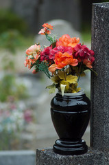 closeup of artificial flowers bouquet in pot on tomb in cemetery