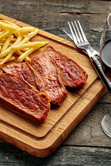 Medium rare sirloin steak with chips and red wine on a rustic wooden table with ethnic tablecloth. Classic European lunch.
