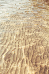 Fototapeta na wymiar Closeup of sea ocean sandy ground with waves ripples. Clear clean shallow warm water of lake river beach in morning or sunset. Natural background with sun light, flare and reflections.