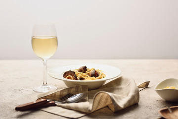 Italian pasta with seafood served with white wine, napkin and cutlery isolated on grey