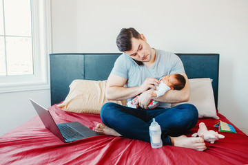 Caucasian father dad with newborn mixed race Asian Chinese baby working from home. Male man parent holding child daughter son talking over phone. Single dad family. Genderblend concept