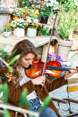 Girl with violin sitting outdoors among flowers