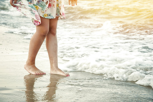 Feet barefoot girl near the water's edge by the sea. A wave rushed over her legs. The concept is a happy childhood. Sea holiday