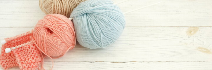 Knitting wool and knitting needles in pastel blue and pink colors on white wooden background...