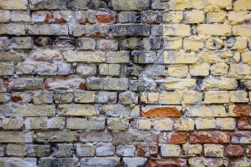 old heavily damaged red brick stone wall with stains of white, yellow and black paint. rough surface texture