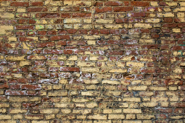 old shabby red brick wall with spots of yellow and white paint. rough surface texture