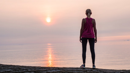 Fototapeta premium Confident fitness woman looking at dawn over the sea, rear view