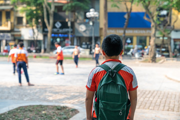 Lonely Asian school boy watches his friends play football outdoor in city