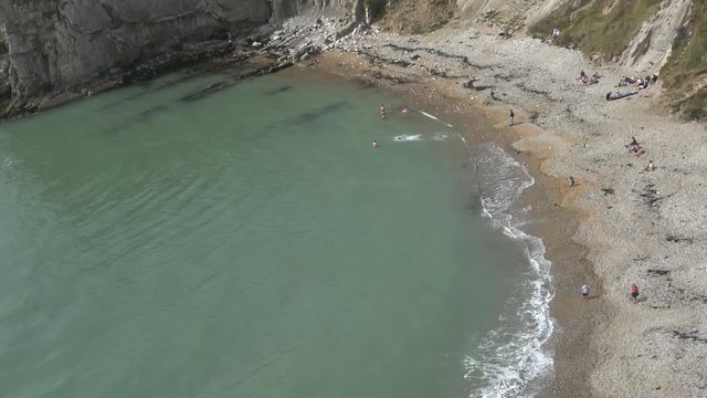 Overhead shot of a beach, a few people standing and some black algae.