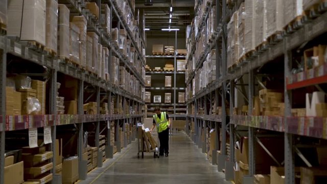 Large huge warehouses with goods, the warehouse worker puts the goods in the cart and looking for new goods on the article using a smartphone, sliding the camera from top to bottom