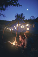 Kids making a small tent with candles and lampions in the backyard.