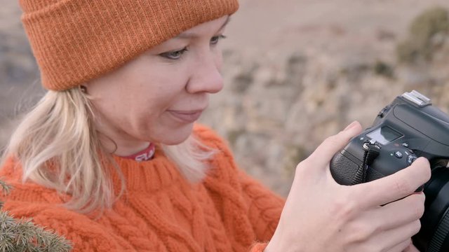 Close-up Girl photographer traveler in an orange sweater and hat takes pictures on his dslr camera landscape on the outdor against the backdrop of epic mountains. Travel Photographers Video Concept