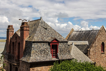 Fototapeta na wymiar View of the top of a picturesque houses in the Mont Saint Michel with seagulls on roofs at sunny day with lovely sky and clouds. Normandie, Nothern France