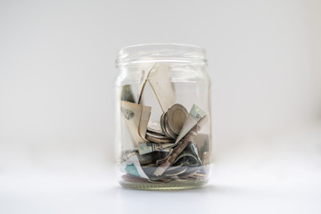 a glass bank with ash money coins and paper ones