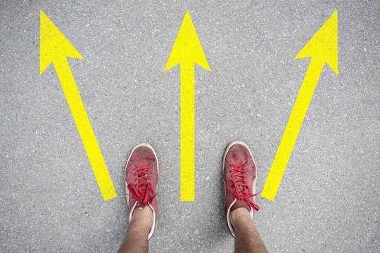 difficult to choose where to go, feet stand on the asphalt abstract surface with arrows