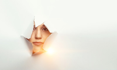 Woman looking out from a hole of torn paper