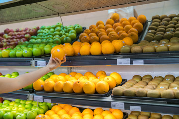 Fresh healthy fruits on shelves in supermarket. With a woman hand choosing best fruits
