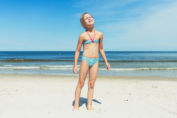 Fototapeta premium Looking into the sun - a little girl on a sandy beach staring straight into the sun