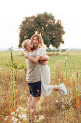 Handsome guy and blonde girl walking on the field on a beautiful warm sunset. gently hug, standing in the sun