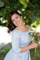 Portrait of romantic young woman with bouquet in retro dress in summer, green trees on the background