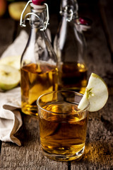 Glass Of Tasty Homemade Apple Cider Two Bottles of Apple Cider Vertical Old Wooden Background Autumn Cold Drink