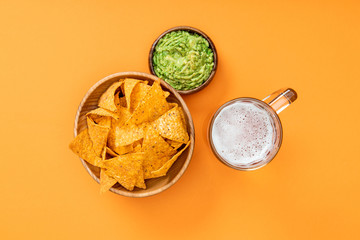 top view of crispy nachos in wooden bowl near guacamole and beer on orange background, Mexican cuisine