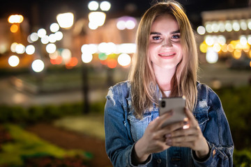 Outdoor portrait of beautiful young woman using her mobile phone at night.